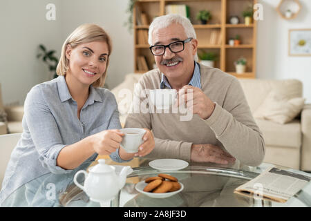 Felice giovane donna e suo padre in pensione tenendo tazze di tè oltre servita tabella Foto Stock