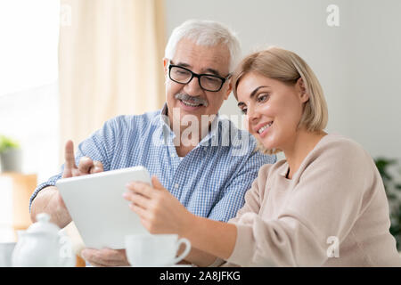 Senior grey-haired l uomo e la sua bella figlia che guarda i video online in tablet Foto Stock