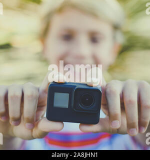 Vista ingrandita di un sorridente teen mediante azione camma. Giovani blogger rendendo video per la storia sociale con GoPro Camera. Studente divertirsi con nuove funzioni multimediali Foto Stock