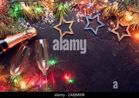 Foto di rami di abete, decorazioni di Natale blu e oro per giocattoli, bruciando le ghirlande, bottiglie di champagne, 2 bicchiere di vino su sfondo nero, posto per Foto Stock