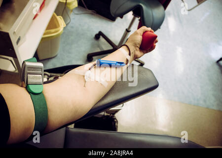 Messa a fuoco selettiva sul braccio di donna mano con ago all'interno della pelle, il sangue che scorre attraverso la donazione di sangue apparecchiature. Felice donna positivo donatore la donazione del sangue c Foto Stock