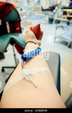 Messa a fuoco selettiva sul braccio di donna mano con ago all'interno della pelle, il sangue che scorre attraverso la donazione di sangue apparecchiature. Felice donna positivo donatore la donazione del sangue c Foto Stock