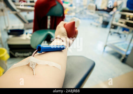 Messa a fuoco selettiva sul braccio di donna mano con ago all'interno della pelle, il sangue che scorre attraverso la donazione di sangue apparecchiature. Felice donna positivo donatore la donazione del sangue c Foto Stock