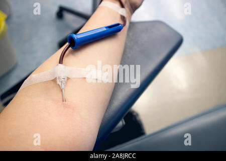 Messa a fuoco selettiva sul braccio di donna mano con ago all'interno della pelle, il sangue che scorre attraverso la donazione di sangue apparecchiature. Felice donna positivo donatore la donazione del sangue c Foto Stock
