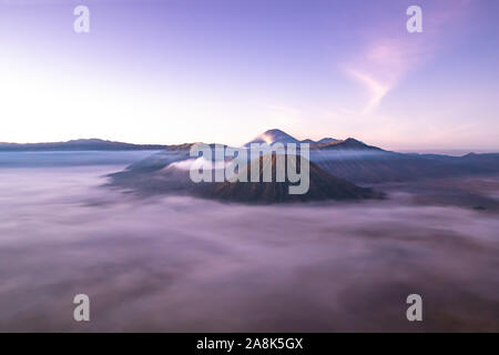 Monte Bromo a sunrise; isola di Giava orientale, Indonesia. Nuvole coperta la valle; fuoriuscite di gas dal cratere. Foto Stock