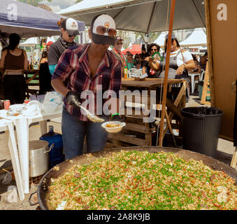 Una signora che la serviva un piatto di paella su una gigantesca padella Foto Stock