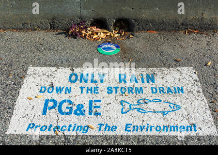 Solo la pioggia giù per storm drain segno di avvertimento PG&E,la Pacific Gas and Electric Company, vicino alla strada di ingresso di scarico. Silhouette di pesce. Proteggere l'ambiente Foto Stock