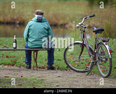 Cottbus, Germania. 6 Nov, 2019. Un uomo anziano si siede da solo su una panchina nel parco e accanto a lui è una bottiglia di birra. Credito: Patrick Pleul/dpa-Zentralbild/ZB/dpa/Alamy Live News Foto Stock