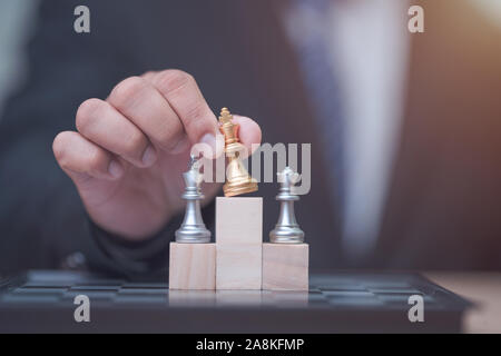 Business man holding golden re scacchi al vincitore posizione sul cubo di legno del gioco degli scacchi Foto Stock