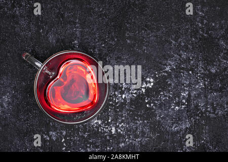 Vista superiore della red hibiscus tea in vetro a forma di cuore sulla tazza tavola nera Foto Stock