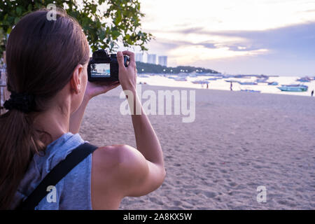 Bella donna di scattare una foto del tramonto. Felice giovane donna con una macchina fotografica e uno zaino. Foto Stock