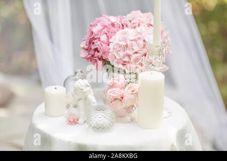 Biglietto di auguri in shabby chic stile. Rosa fiori di ortensie, statuetta di un angelo, marshmallows, candele sul tavolo. Foto Stock