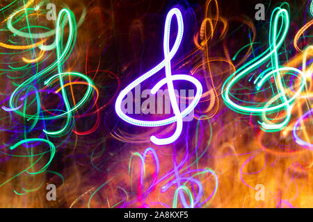 Close-up molto neon multicolore incandescente treble clefs. Abstract sfondo luminoso. Effetto fotografico di lunga esposizione. Foto Stock