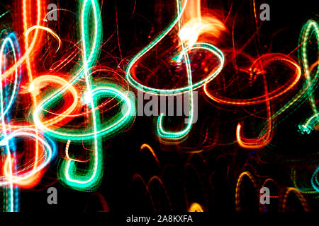 Close-up di colore rosso e verde neon incandescente treble clefs. Abstract sfondo luminoso. Effetto fotografico di lunga esposizione. Foto Stock