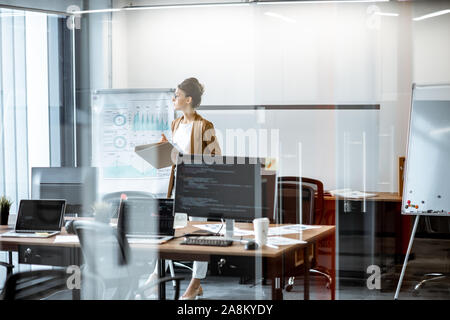 Giovane donna d'affari in preparazione per una presentazione, in piedi da solo con i documenti nei pressi di lavagna a fogli mobili in ufficio moderno o coworking space Foto Stock