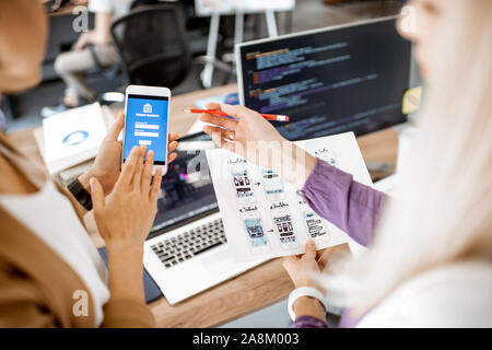 Gli sviluppatori o progettisti web sviluppo applicazione mobile per il settore bancario in ufficio, close-up sul telefono e schizzi di carta Foto Stock