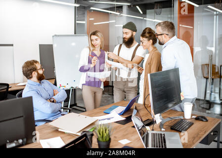 Gruppo di diversi colleghi che lavorano in uffici moderni, avendo discussioni o sale conferenza di piccole dimensioni su un posto di lavoro con computer Foto Stock