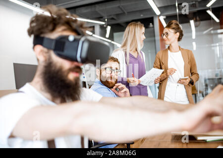 Giovani che lavorano in ufficio, creative uomo barbuto cercando un nuovo prodotto o un nuovo gioco di realtà virtuale gli occhiali di protezione Foto Stock