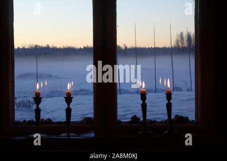 Quattro candele in un tradizionale vecchio finestra. Fuori è un rurale paesaggio invernale, cielo blu e del crepuscolo. La lana di pecora è utilizzato come decorazione tra esterno un Foto Stock