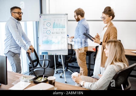 Gruppo di diversi colleghi a discutere di alcuni momets lavoro con presentazione su lavagna nel corso di una piccola conferenza in ufficio Foto Stock