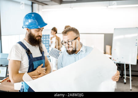 Senior caposquadra e operaio in tuta a lavorare sul progetto con blueprint in ufficio Foto Stock