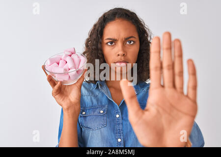 Giovane donna brasiliana tenendo la coppa con marshmallows isolato su sfondo bianco con mano aperta facendo segno di stop con gravi e fiducioso expressi Foto Stock