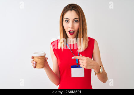 Redhead imprenditrice indossando la scheda id bere tazza di caffè isolato su sfondo bianco molto felice puntando con mani e dita Foto Stock