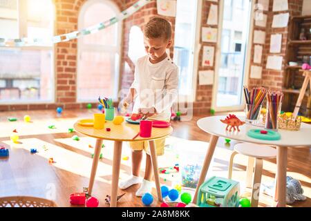 Bella bionda toddler giocando in plastica con cibi e piatti. Piedi intorno un sacco di giocattoli a kindergarten Foto Stock