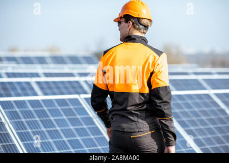 Ben attrezzato lavoratore in arancione di protezione abbigliamento esaminando i pannelli solari su un tetto fotovoltaico impianto. Concetto di manutenzione e installazione di stazioni solari Foto Stock