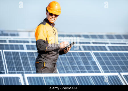 Ingegnere in indumenti da lavoro protettiva di effettuare servizio di pannelli solari con tavoletta digitale su un tetto fotovoltaico impianto. Concetto di manutenzione e configurazione di energia solare stazione Foto Stock