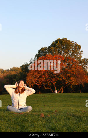 Felice ragazza adolescente con cuffie ascolta la musica dal suo smartphone nel parco soleggiata giornata autunnale Foto Stock