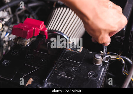 Mano del servizio tecnico di controllare la batteria e ruotare la batteria vite allentata in garage Foto Stock