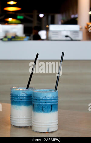 Due bicchieri di pisello ghiacciata del latte. Tè blu cocktail a strati con il latte sul tavolo di legno nero con paglia e ghiaccio. Analcolica morbida e sana bevanda fredda. Foto Stock