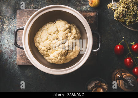 Tutto il cavolfiore in pentola di cottura su scuro dello sfondo rustico con ingredienti. Vista superiore Foto Stock