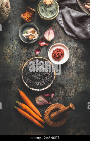 Nero con le lenticchie di cottura Ingredienti per gustosi piatti vegan su sfondo scuro. Vista dall'alto. Salutare mangiare vegetariano concetto. Banner orizzontale. Piano Foto Stock