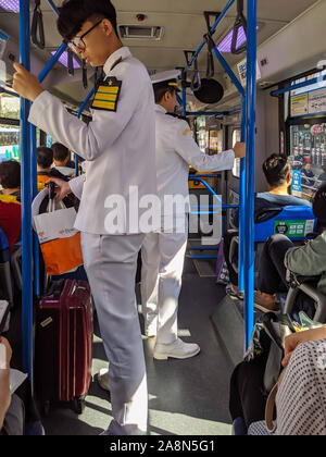 SEPT. 13, 2019-BUSAN COREA DEL SUD : interno di un trasporto pubblico di passeggeri seduti e due colleghi asiatici bianco che indossano uniformi marine standi Foto Stock