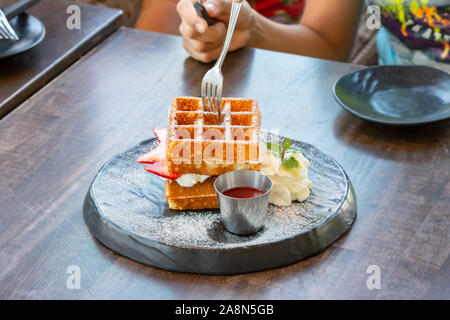 Waffle Strawerry panna fresca nella piastra nera su un tavolo di legno. Foto Stock