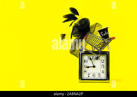 Venerdì nero vendita concetto con orologio argento, carrello con segno vendita e femmina hat in stile retrò su sfondo giallo. Pianificazione del tempo, copia dello spazio. Il concetto di partito. Natale layout vintage. Foto Stock