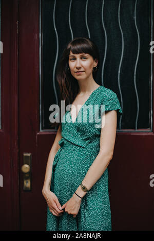 Donna che indossa un elegante abito verde è in piedi di fronte a porta rossa Foto Stock
