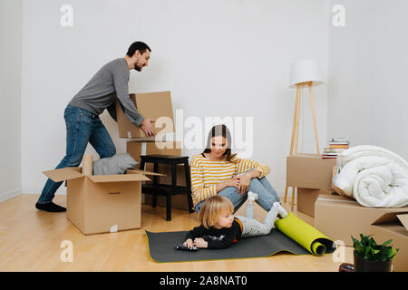 La famiglia felice di passare a una nuova casa, ragazzo gioca con i giocattoli mentre i genitori disimballare Foto Stock
