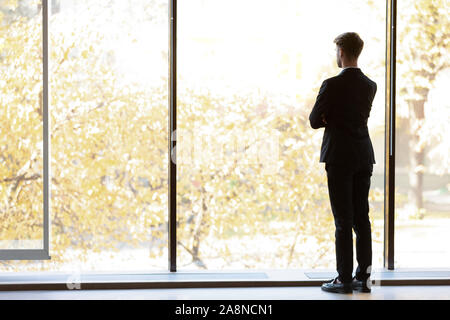 Vista posteriore di imprenditore cercare nel pensiero di distanza Foto Stock