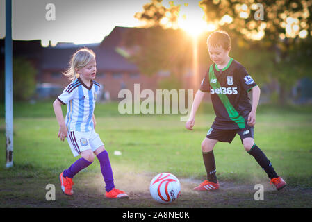 Un ragazzino con autismo, ADHD, sindrome di Asperger e sua sorella più piccola a giocare a calcio nel parco al tramonto, Stoke City e kit di Argentina su Foto Stock