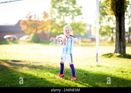 Un ragazzino con autismo, ADHD, sindrome di Asperger e sua sorella più piccola a giocare a calcio nel parco al tramonto, Stoke City e kit di Argentina su Foto Stock