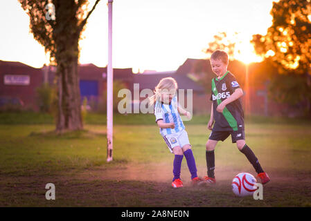 Un ragazzino con autismo, ADHD, sindrome di Asperger e sua sorella più piccola a giocare a calcio nel parco al tramonto, Stoke City e kit di Argentina su Foto Stock