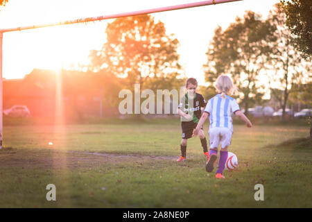 Un ragazzino con autismo, ADHD, sindrome di Asperger e sua sorella più piccola a giocare a calcio nel parco al tramonto, Stoke City e kit di Argentina su Foto Stock