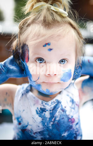 Un adorabile piccolo bambino, ragazza è divertente giocare con la colorazione di pitture, getting confuso e divertirsi un sacco, girato in un ambiente domestico Foto Stock