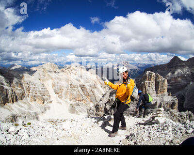 Un felice donna attraente alpinista dà un pollice in alto su un picco di montagna nelle Dolomiti Foto Stock