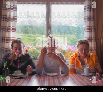 Vista di tre donne giovani alpinisti gustare un caffè caldo in un rifugio dopo una dura salita Foto Stock