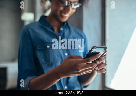 Imprenditrice in piedi in ufficio e utilizzando il suo telefono cellulare. Focus su smart phone in mano a una donna che indossa casuals. Foto Stock