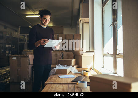 Giovane con una carta in mano in piedi dalla zona di confezionamento in ufficio. Online store proprietario lavora in ufficio. Foto Stock